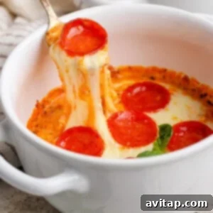 A spoon lifting a portion of gooey, cheesy pepperoni pizza dip from a white bowl, with fresh basil leaves visible nearby, indicating it's ready to enjoy.
