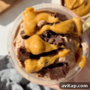 A bowl of chocolate ice cream topped with caramel sauce and chunks of chocolate brownies. A gold spoon is partially visible on the right.