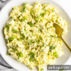 A bowl of egg salad with chopped green onions and dill, accompanied by a gold spoon, ready to be served.