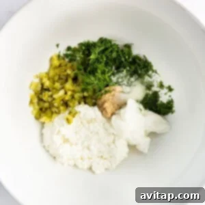 A white bowl holds a creamy mixture of cottage cheese, chopped pickles, fresh dill, and seasonings, ready for the next step.
