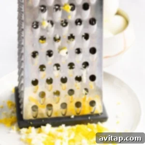 A metal cheese grater rests on a white plate with finely grated egg, next to a bowl of whole boiled eggs, illustrating the grating technique.