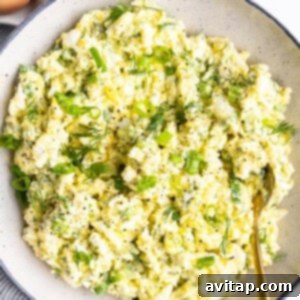 A bowl of egg salad with chopped green onions and dill, seasoned with black pepper. Three whole eggs are in the background, completing the picture.
