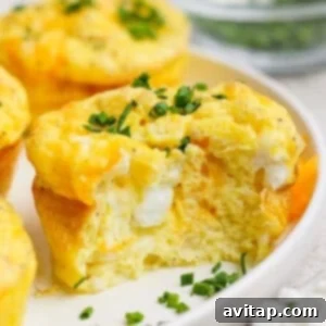 A baked egg muffin with a bite taken out, showing a fluffy texture and cheese inside, topped with chopped green onions on a white plate.