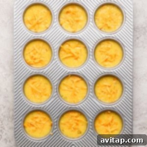 Muffin tin filled with unbaked batter topped with shredded cheese, ready for baking.