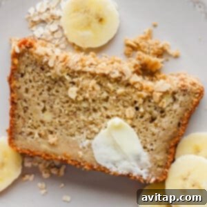 Wholesome Oat Banana Loaf 5 A perfectly portioned slice of banana bread, generously topped with butter and oats, encircled by fresh banana slices, all arranged on a pristine white plate, ready to be enjoyed.