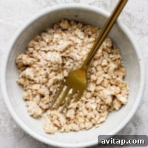Wholesome Oat Banana Loaf 6 A bowl of dry oatmeal mixture with a gold fork placed inside on a textured surface, ready for streusel preparation.