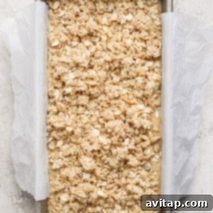 Wholesome Oat Banana Loaf 9 A rectangular baking dish lined with parchment paper contains an unbaked oat crumble mixture, ready for the oven on a light textured surface, highlighting the streusel topping.