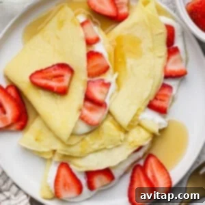 Creamy Cottage Cheese Crepes 6 Crepes folded and topped with sliced strawberries, cream, and syrup on a white plate.