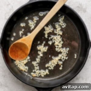 A cast iron skillet with sautéing minced garlic in oil, accompanied by a wooden spoon.