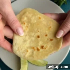 Two hands hold a flatbread over a plate containing lime wedges.