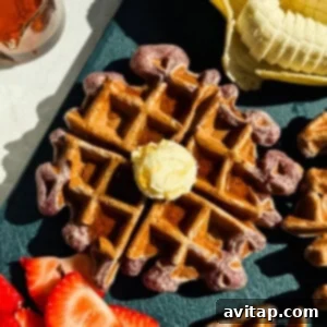 A waffle topped with a dollop of butter is surrounded by sliced bananas and strawberries on a dark surface.
