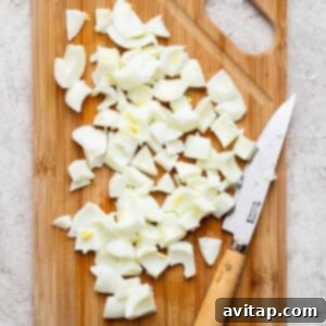 Chopped boiled eggs neatly arranged on a wooden cutting board with a knife resting beside them, positioned on a light-colored kitchen surface.
