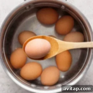 Eggs being carefully placed into a pot of boiling water, steam rising from the surface, indicating the cooking process for perfectly hard-boiled eggs.