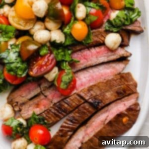 A perfectly seared and sliced medium-rare steak served with a vibrant Caprese salad of cherry tomatoes, mozzarella balls, and fresh basil on a white plate, showcasing a delightful meal.