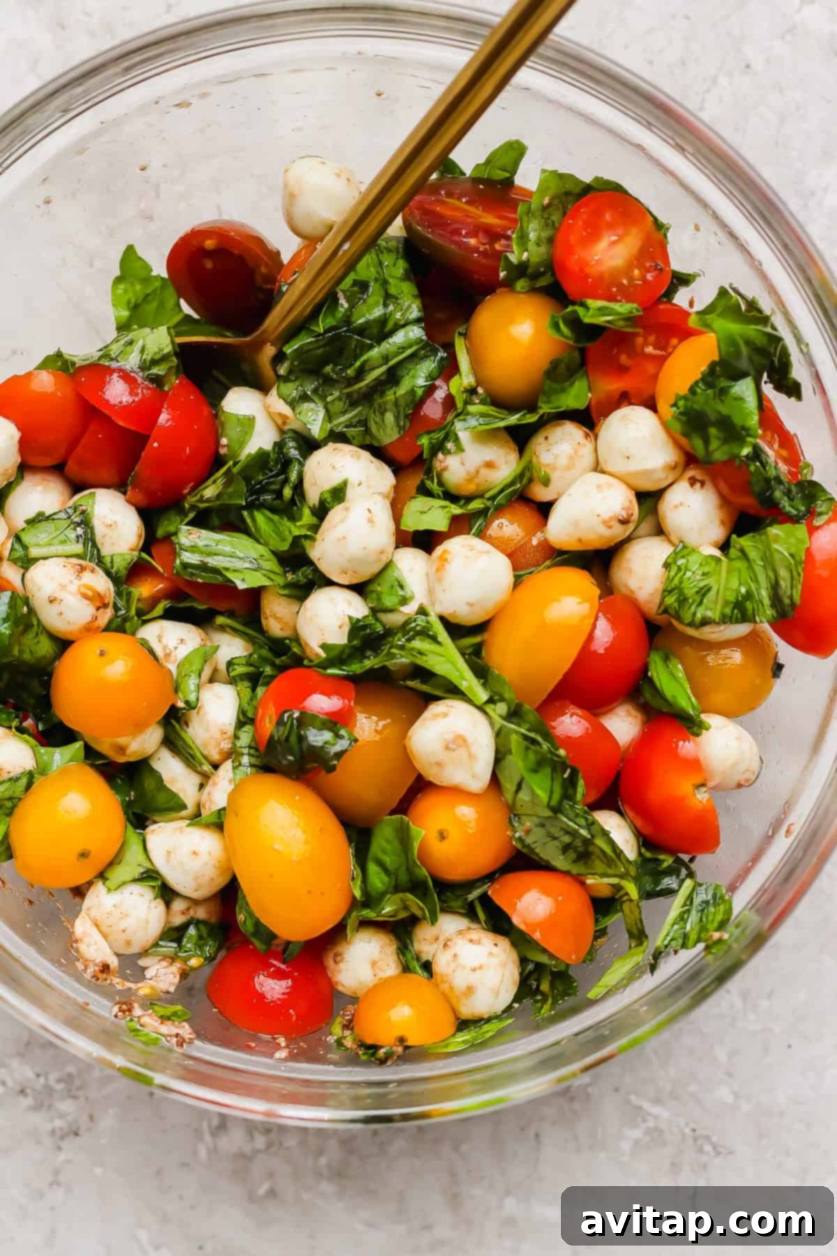A clear glass bowl generously filled with vibrant cherry tomatoes, creamy mozzarella balls, and aromatic fresh basil leaves, ready for the Caprese topping, resting on a rustic light surface.