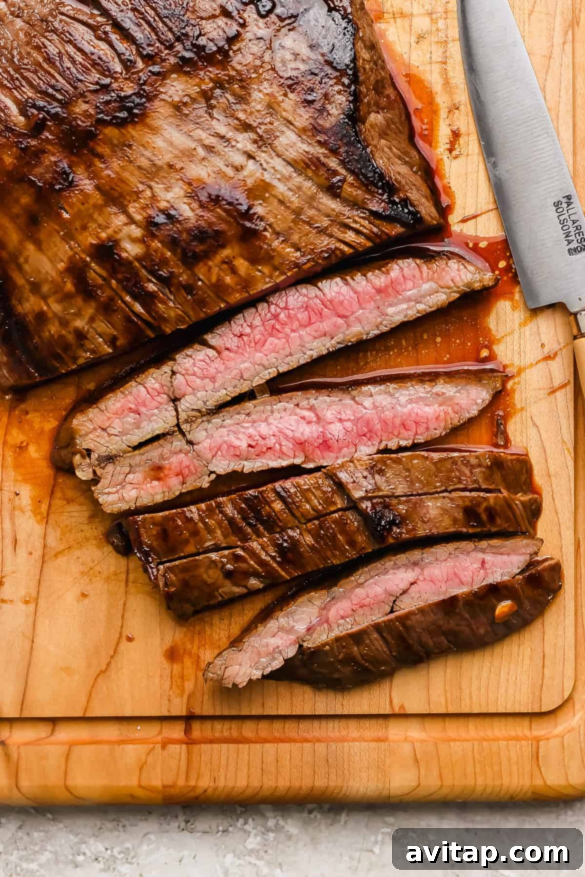 Perfectly sliced medium-rare balsamic skirt steak arranged on a rustic wooden cutting board, accompanied by a sharp chef's knife, ready for serving.