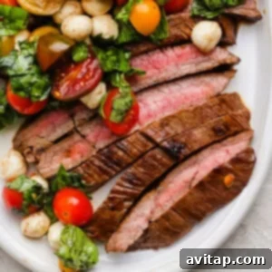 Sliced medium-rare balsamic skirt steak served with a vibrant caprese salad of cherry tomatoes, mozzarella balls, and fresh basil on a pristine white plate.