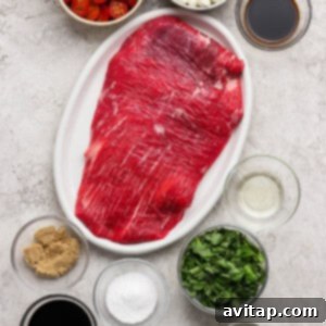 Raw flank steak on a white plate surrounded by bowls of grape tomatoes, mozzarella balls, brown sugar, spinach, balsamic vinegar, Worcestershire sauce, salt, olive oil, mustard, and garlic, ready for preparation.