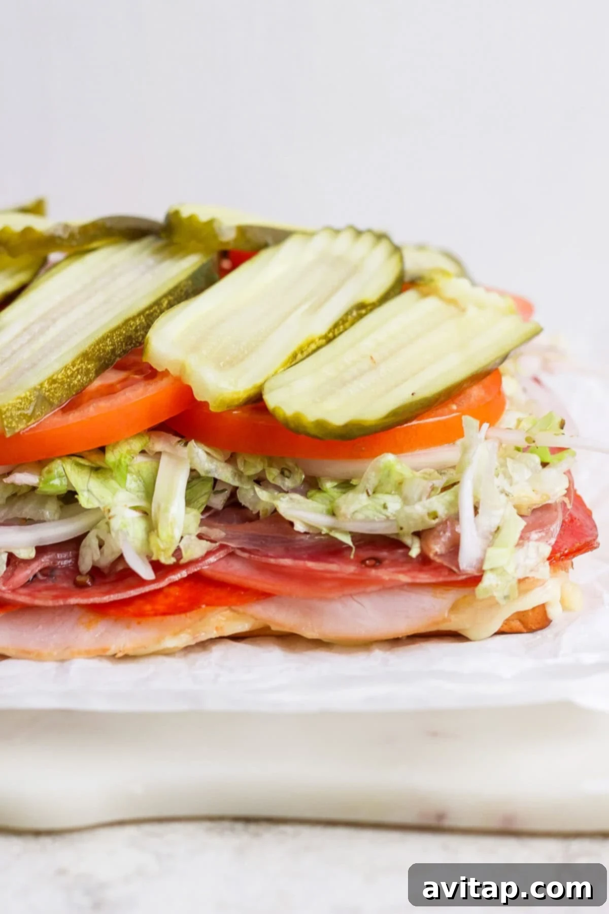 A close-up of an Italian grinder slider with layers of premium deli meats, melted cheese, fresh shredded lettuce, and ripe tomatoes, all nestled in a soft, golden Hawaiian roll.