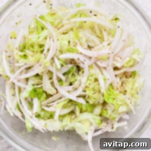 A clear glass bowl filled with vibrant shredded lettuce and thinly sliced onions, seasoned and mixed with olive oil, ready to top the baked Italian grinder sliders.
