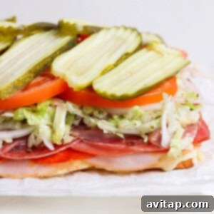Preparing the Italian Grinder Sliders with fresh toppings. The top bun is gently removed, revealing melted cheese and deli meats, with fresh lettuce, tomatoes, and pickles being carefully added before replacing the bun.