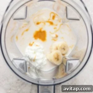 A blender containing milk, sliced banana, cottage cheese, and a drizzle of honey, viewed from above.