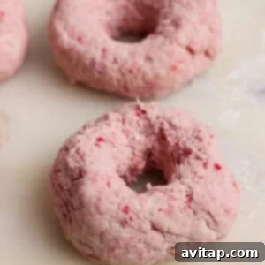 Creamy Strawberry Cottage Bagels 10 Two unbaked, pinkish doughnuts made with a textured dough rest on a light-colored surface.