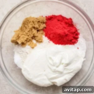 Creamy Strawberry Cottage Bagels 7 A glass bowl containing flour, brown sugar, white sugar, red powder, and a dollop of yogurt on a light surface.