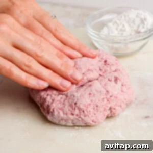 Creamy Strawberry Cottage Bagels 8 A person kneads pink dough on a floured surface with a bowl of flour in the background.