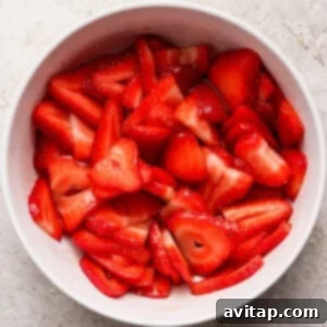 A white bowl filled with sliced fresh strawberries sits on a light textured surface.