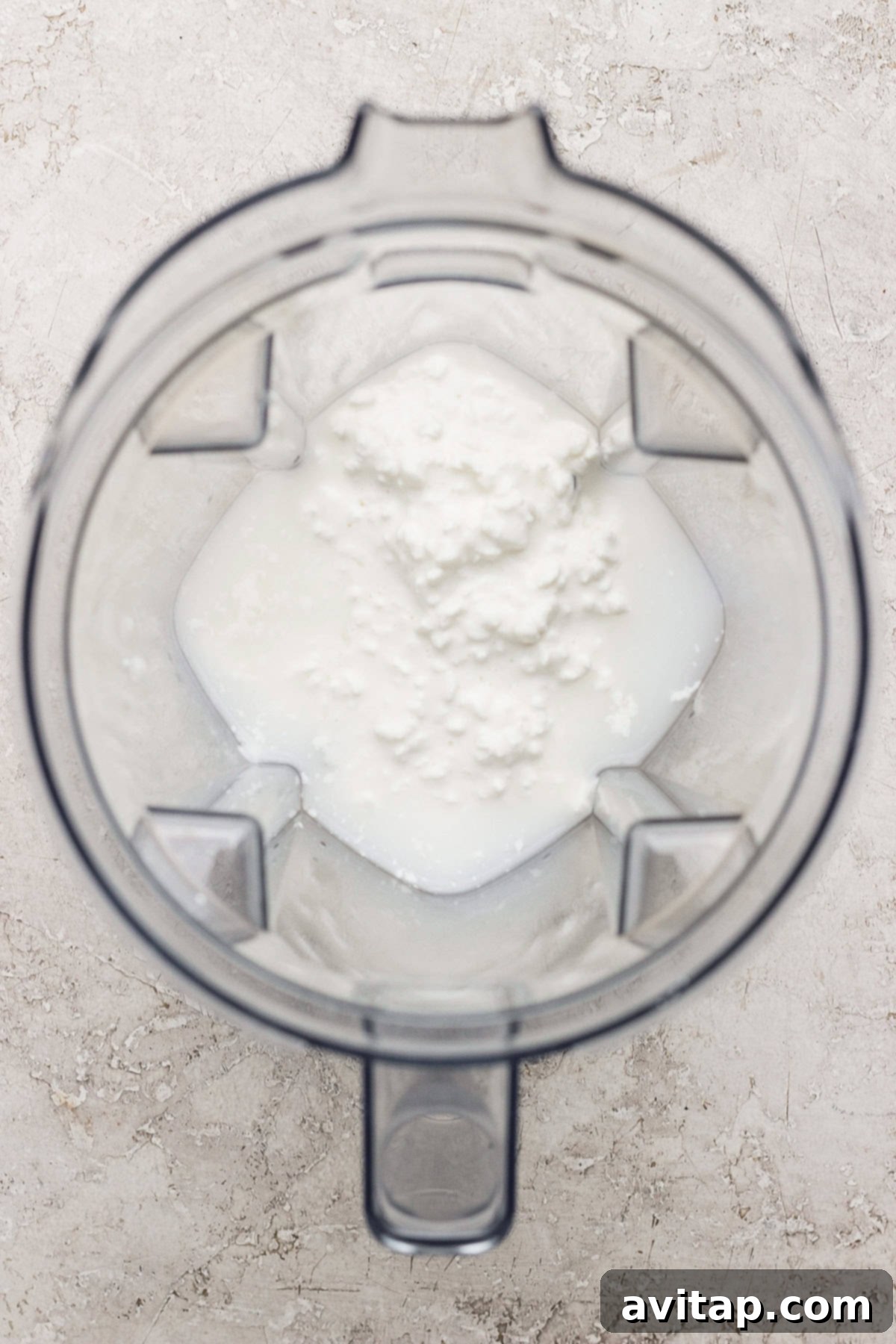 Blender jug with foamy white liquid inside, viewed from above.