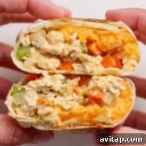 Two hands hold a halved breakfast burrito filled with scrambled eggs, cheese, onions, green peppers, and orange bell peppers.