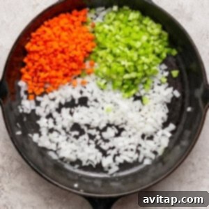 A cast iron skillet containing diced carrots, celery, and onions arranged in separate sections on a light textured surface.