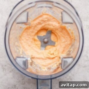 A blender with creamy, light orange mixture spread around the blades, viewed from above on a textured surface.