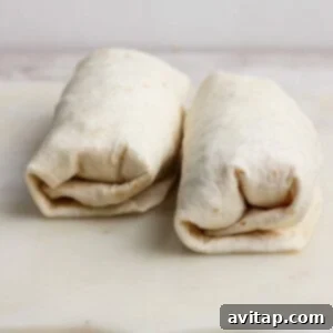 Two neatly wrapped burritos placed side by side on a white cutting board.