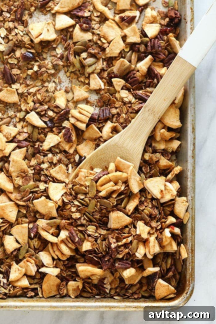 Golden brown apple cinnamon granola spread on a baking sheet, fresh out of the oven.
