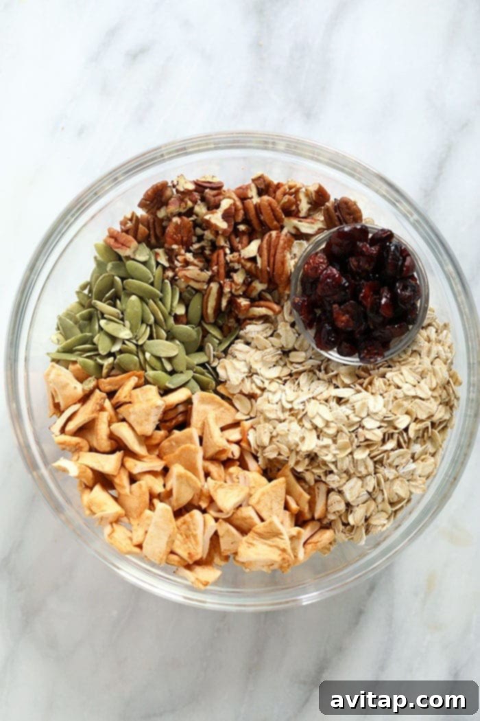 A bowl filled with the dry ingredients for apple cinnamon granola, including oats, walnuts, and pepitas, ready to be mixed.