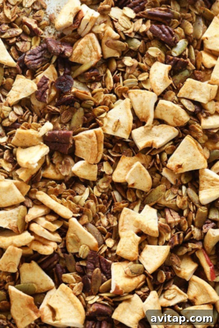 Freshly baked apple cinnamon granola cooling on a baking sheet, showcasing golden clusters and dried fruit.