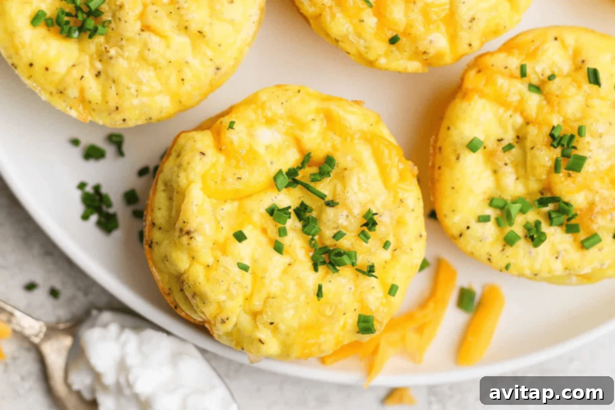 Cozy Fall Protein: Cottage Cheese Delights 5 Three baked egg muffins topped with chopped chives sit on a white plate, with shredded cheese and a spoonful of cottage cheese nearby, illustrating a healthy breakfast.