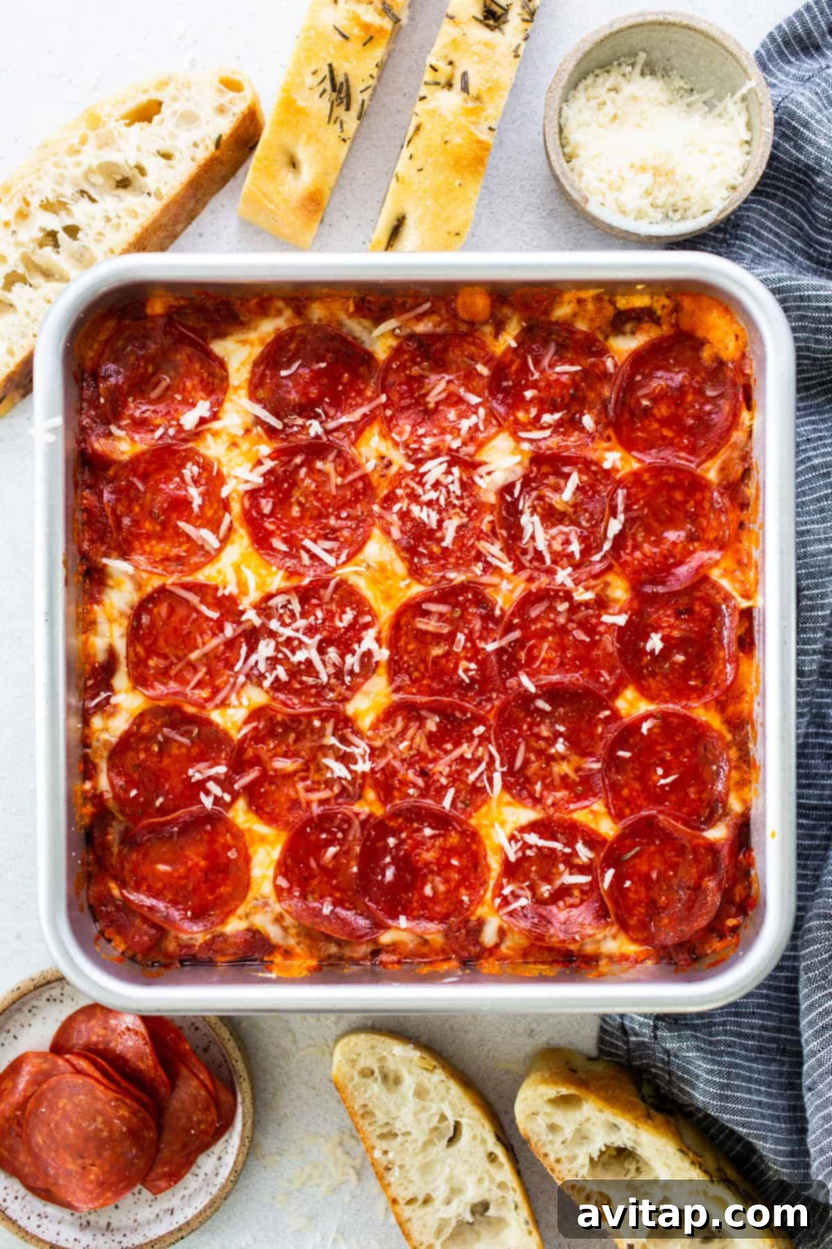 Cozy Fall Protein: Cottage Cheese Delights 6 Square deep-dish pepperoni pizza in a pan, surrounded by bread slices, grated cheese in a bowl, and a small plate of pepperoni slices on a light surface, showcasing a pizza dip or appetizer setup.