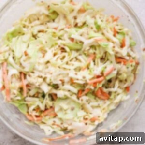 A glass bowl filled with coleslaw made of shredded cabbage and carrots on a light, textured surface.