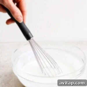 A person whisking milk and other ingredients in a glass bowl.