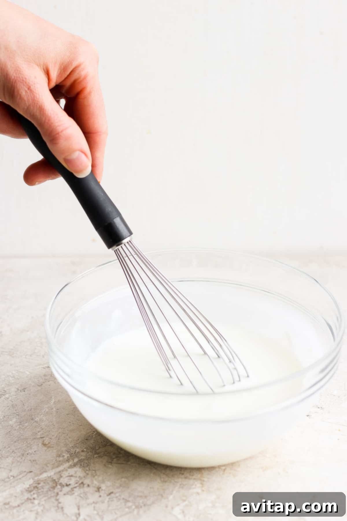 A person whisking creamy ranch dressing in a glass bowl.