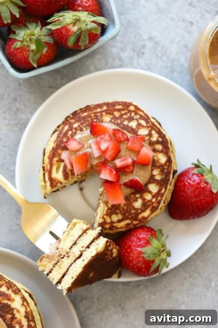 Top-down view of stacked Almond Flour Banana Pancakes garnished with fresh strawberry slices and a drizzle of maple syrup.