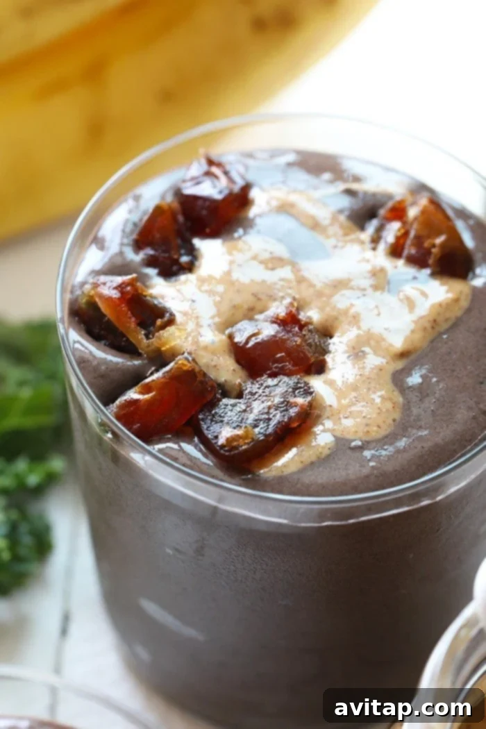 Close-up of a Dark Chocolate Date Protein Smoothie in a tall glass, garnished with chopped dates and a spoon, showcasing its rich, creamy texture.