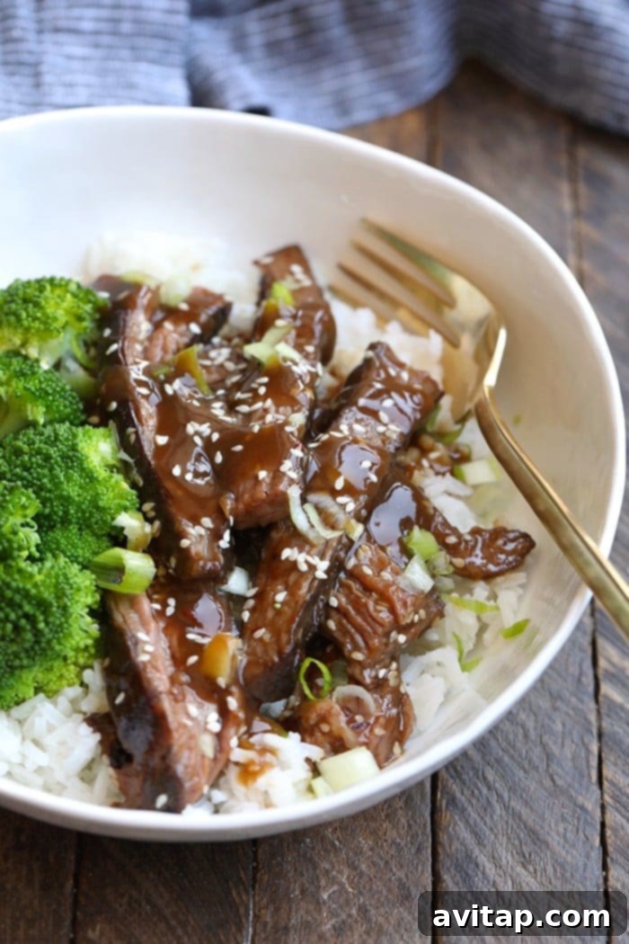 sous vide steak on rice, a perfectly cooked flank steak served over a bed of fluffy white rice, garnished with green onions and a drizzle of rich Mongolian sauce, showcasing the tender interior of the meat.