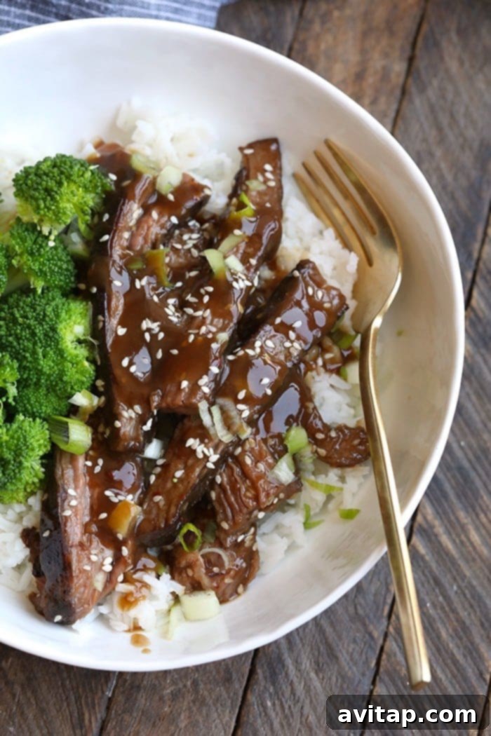 A beautifully presented dish of Mongolian Sous Vide Flank Steak, sliced and served over a bed of white rice, garnished with fresh green onions and sesame seeds, highlighting the rich sauce.