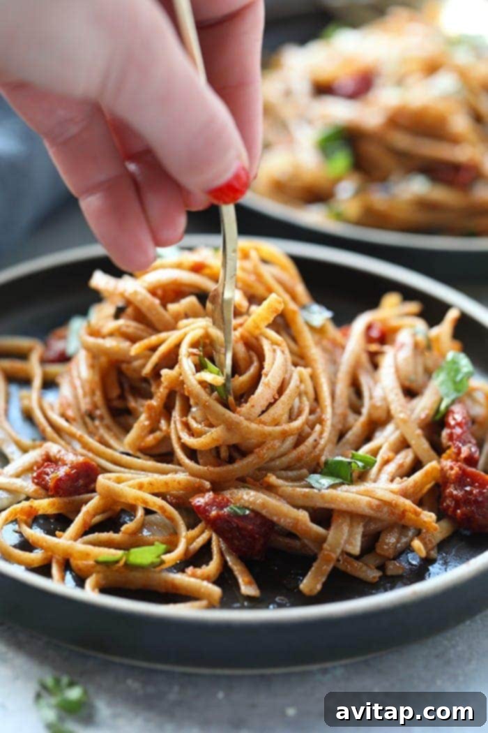 Twirling Delicious Whole Wheat Sun-Dried Tomato Pasta Close-up of whole wheat sun-dried tomato pasta perfectly twirled on a fork, showcasing its vibrant color and fresh ingredients.