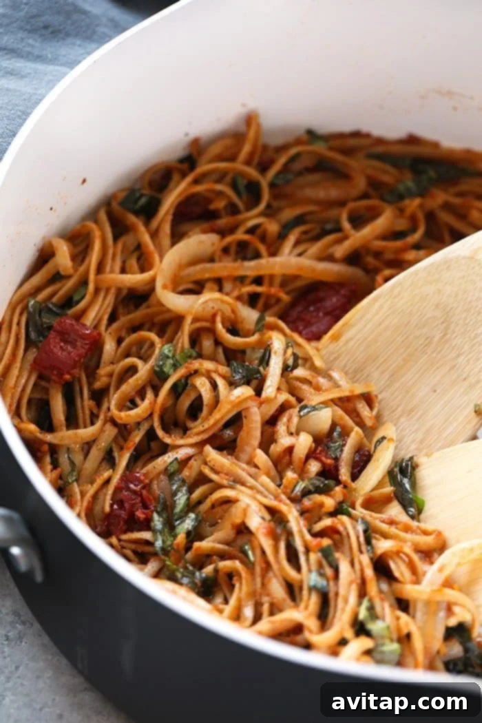 Cooking Whole Wheat Sun-Dried Tomato Pasta in a Skillet Whole wheat sun-dried tomato pasta being tossed with sauce and onions in a large pan, highlighting the cooking process.