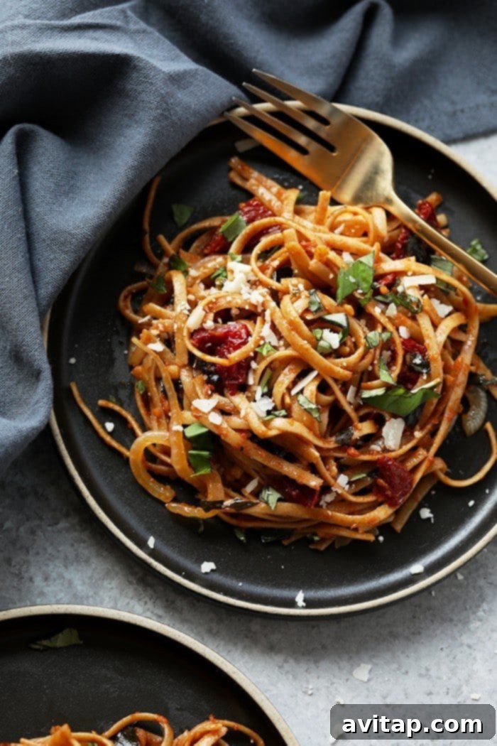 Garnishing Vegetarian Sun-Dried Tomato Pasta with Parmesan Close-up of vegetarian sun-dried tomato pasta garnished with fresh Parmesan cheese and basil, ready for serving.